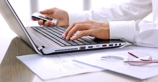 blog picture of laptop keyboard and a man's left hand on keys and right hand holding cell phone