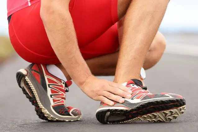 Male athlete massages his foot due to ankle pain.